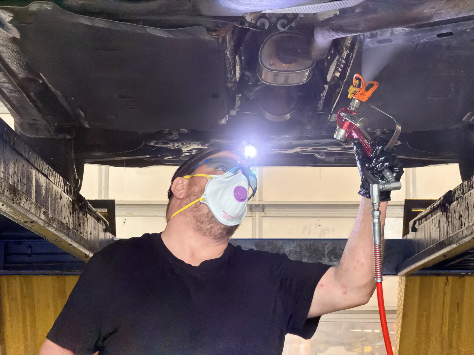Technician applying the rust protection treatment underneath a vehicle raised on the shop hoist